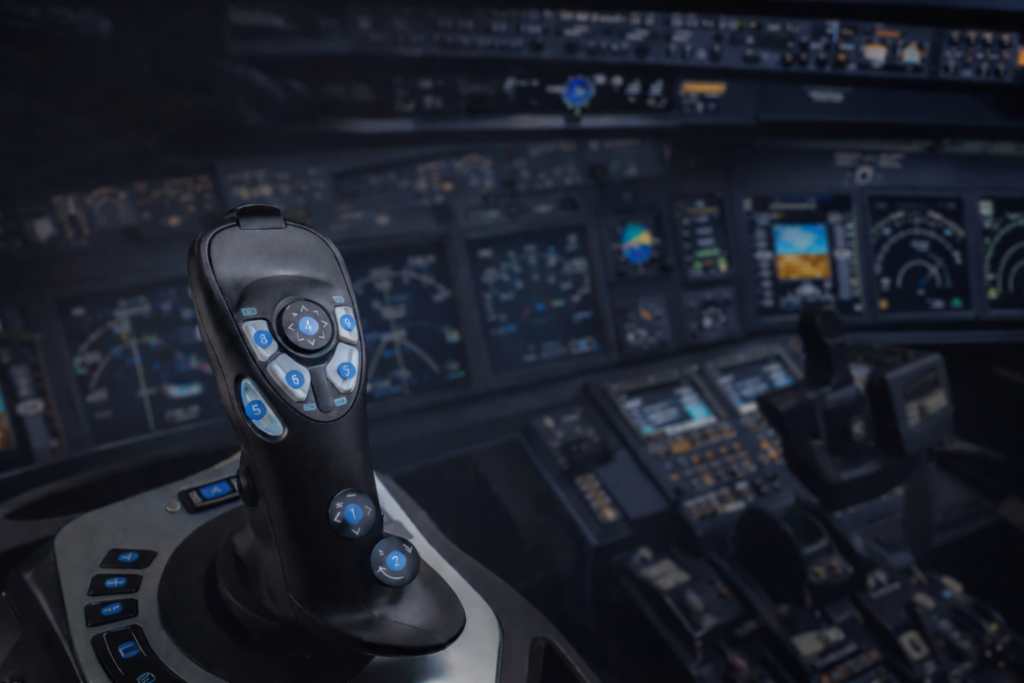 flight simulator joystick in cockpit setup with illuminated controls and blurred instrument panel background.